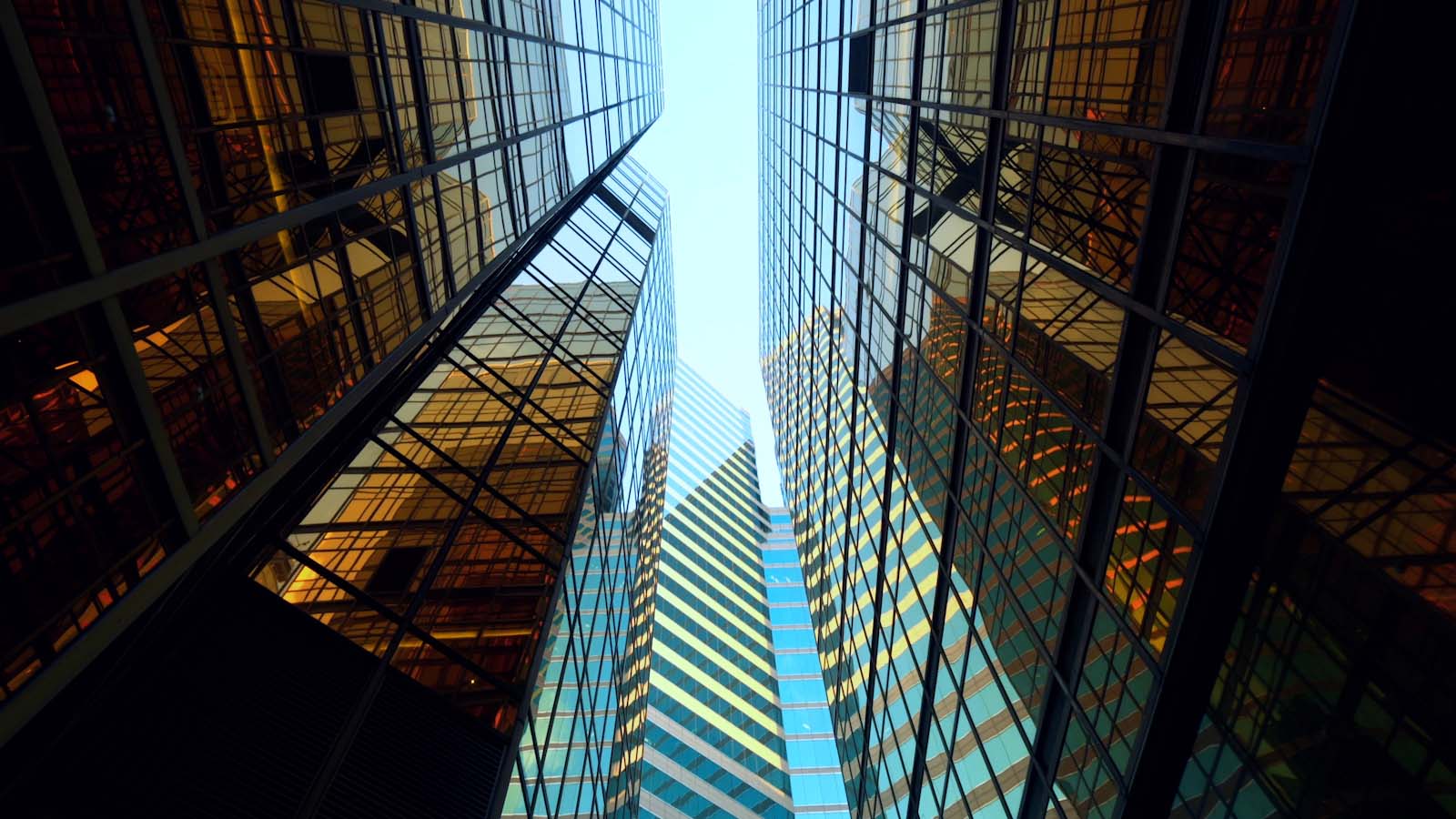 Eine Perspektive von unten zeigt mehrere moderne Hochhäuser mit großen Glasfassaden, die das Licht reflektieren.