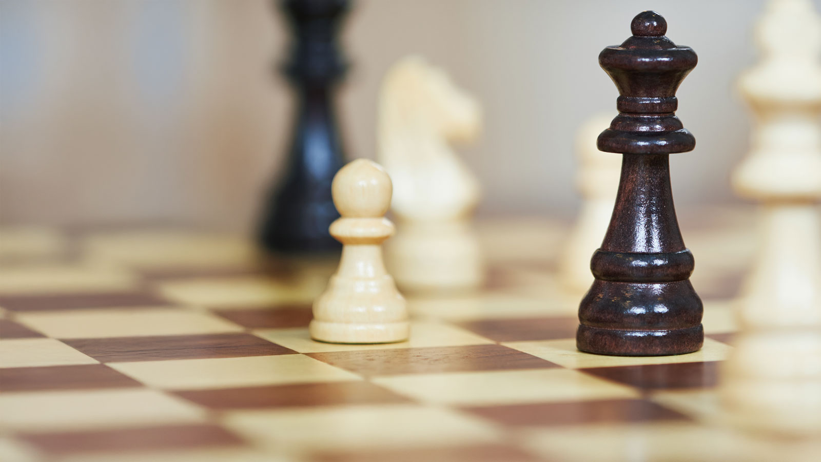 Nahaufnahme einer Schachpartie mit Schachfiguren aus Holz. Der schwarze König steht im Vordergrund auf einem Schachbrett, umgeben von weißen und schwarzen Spielfiguren.