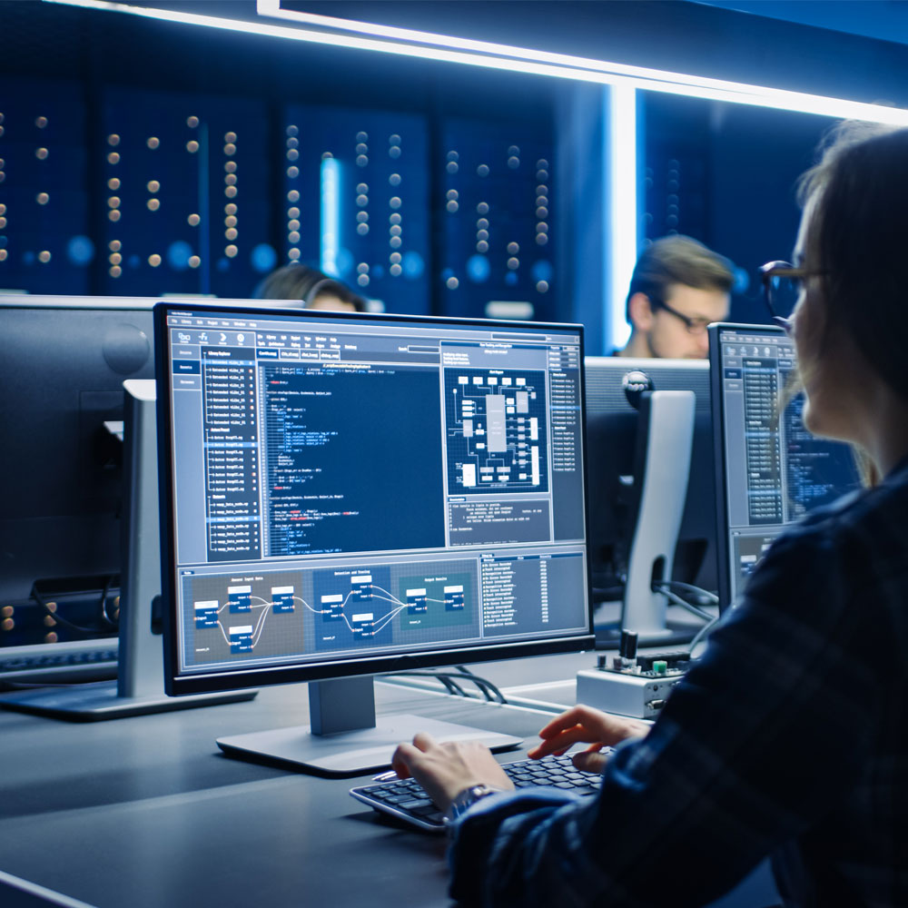 Person arbeitet an Computer mit Programmiercode und Diagrammen auf dem Bildschirm in einem modernen Büro.