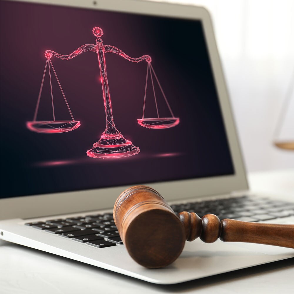 Ein Richterhammer liegt auf der Tastatur eines Laptops, auf dessen Bildschirm eine digitale Waage der Gerechtigkeit in leuchtendem Rot dargestellt ist.