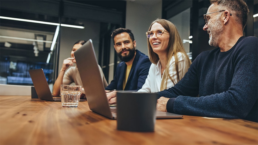 Several people sitting at a conference table with open laptops in a modern office.