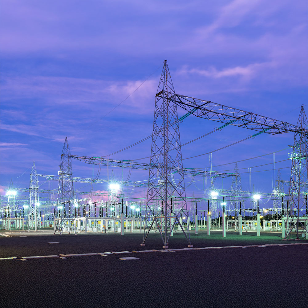 Electrical substation with high-voltage towers and illuminated equipment at dusk.