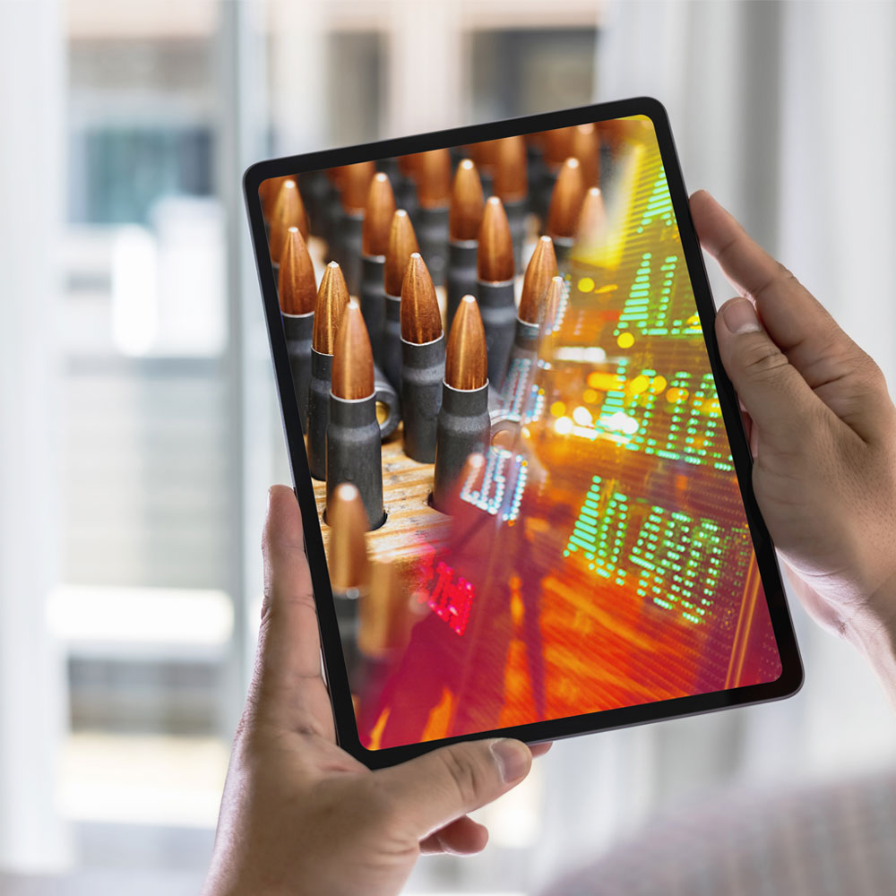 Hands holding a tablet displaying ammunition and stock market data.