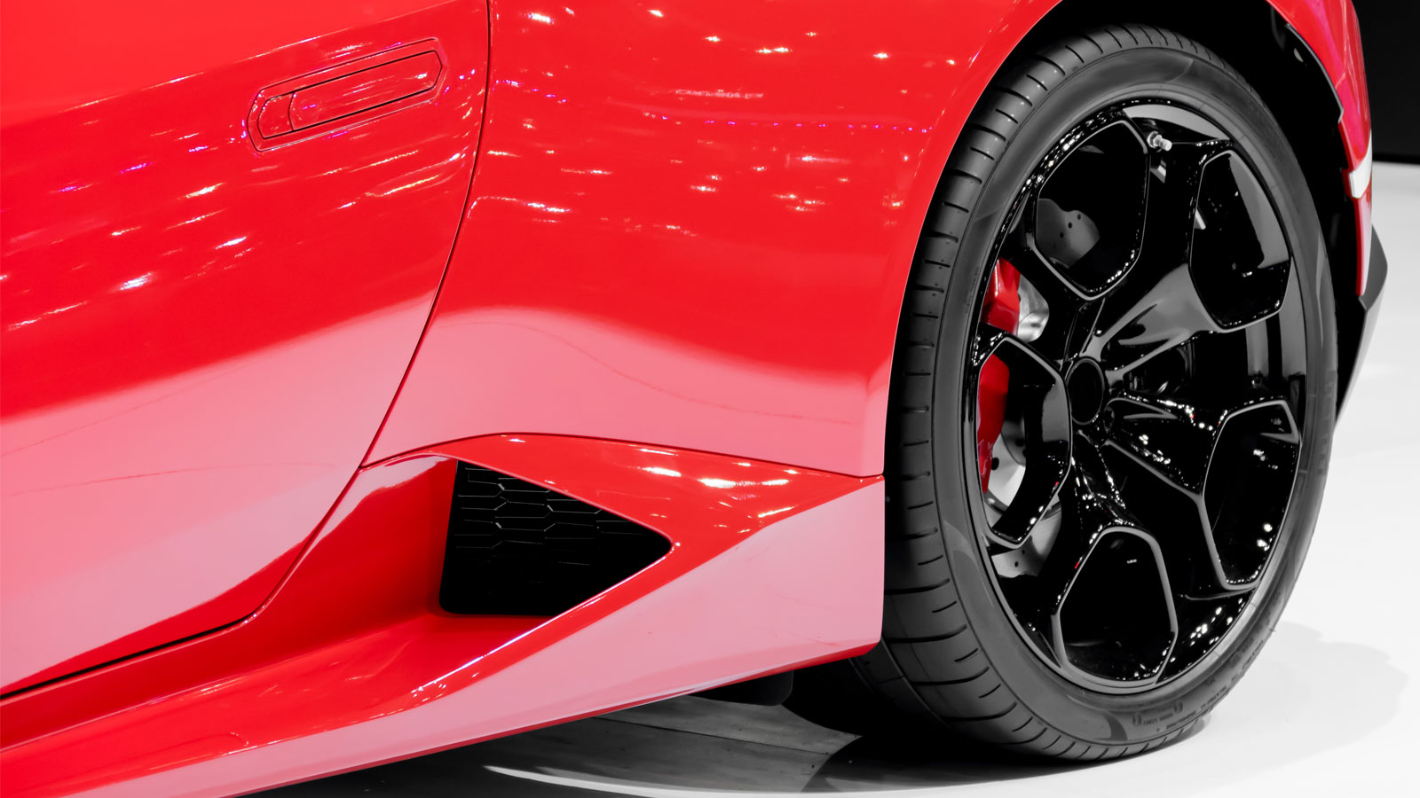 A close-up image captures the vibrant design of a red sports car featuring sleek, glossy black wheels. 
