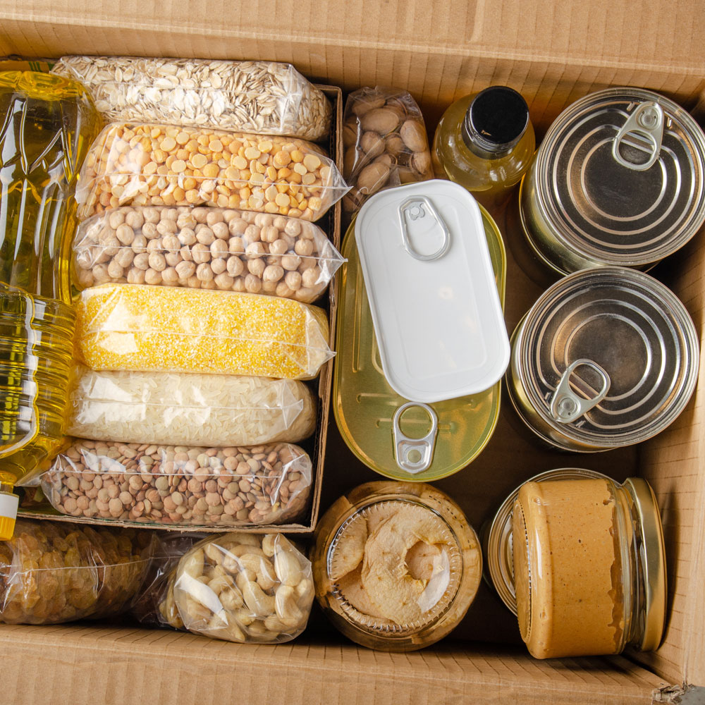 Box with various shelf-stable foods like oil, legumes, cans, and jars.