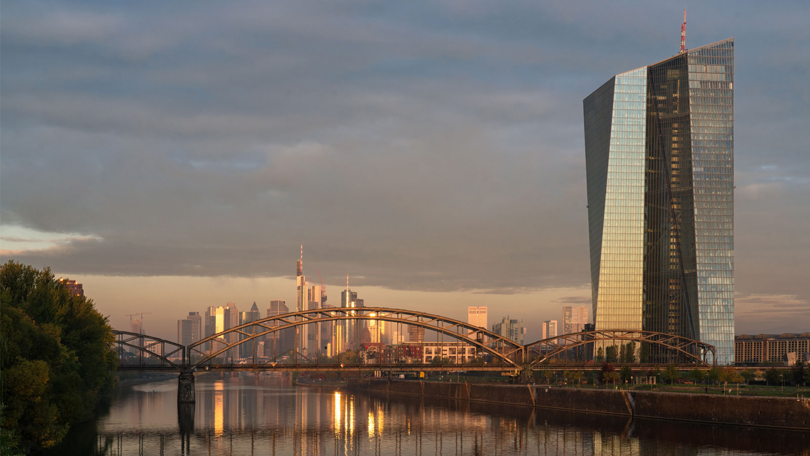Frankfurt skyline with the European Central Bank and a bridge over the Main River at sunset.
