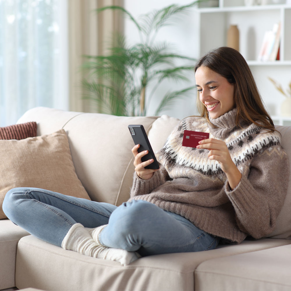 Woman sitting on a sofa holding a smartphone and a credit card.