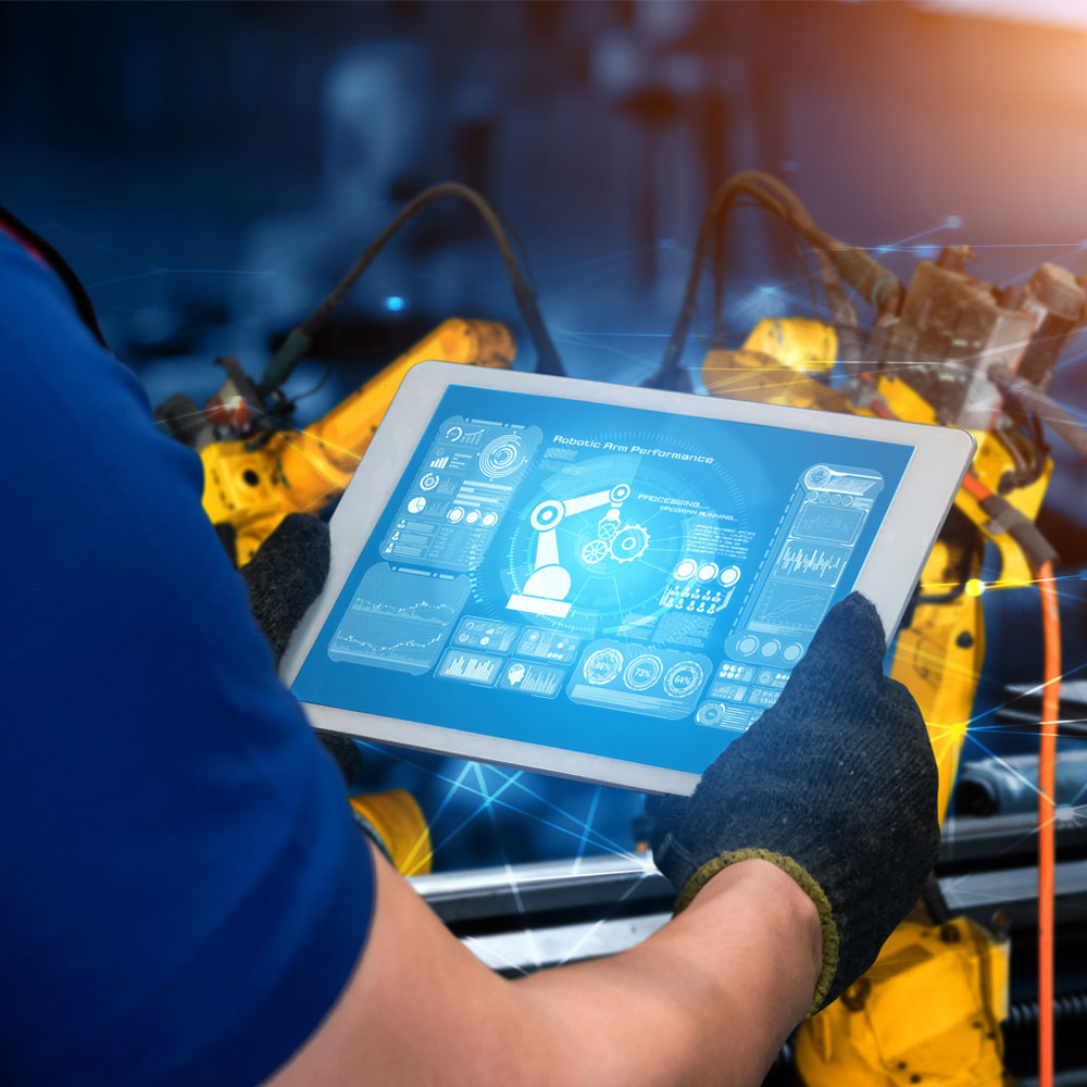 Engineer wearing gloves operates a tablet to control yellow industrial robots in a factory.