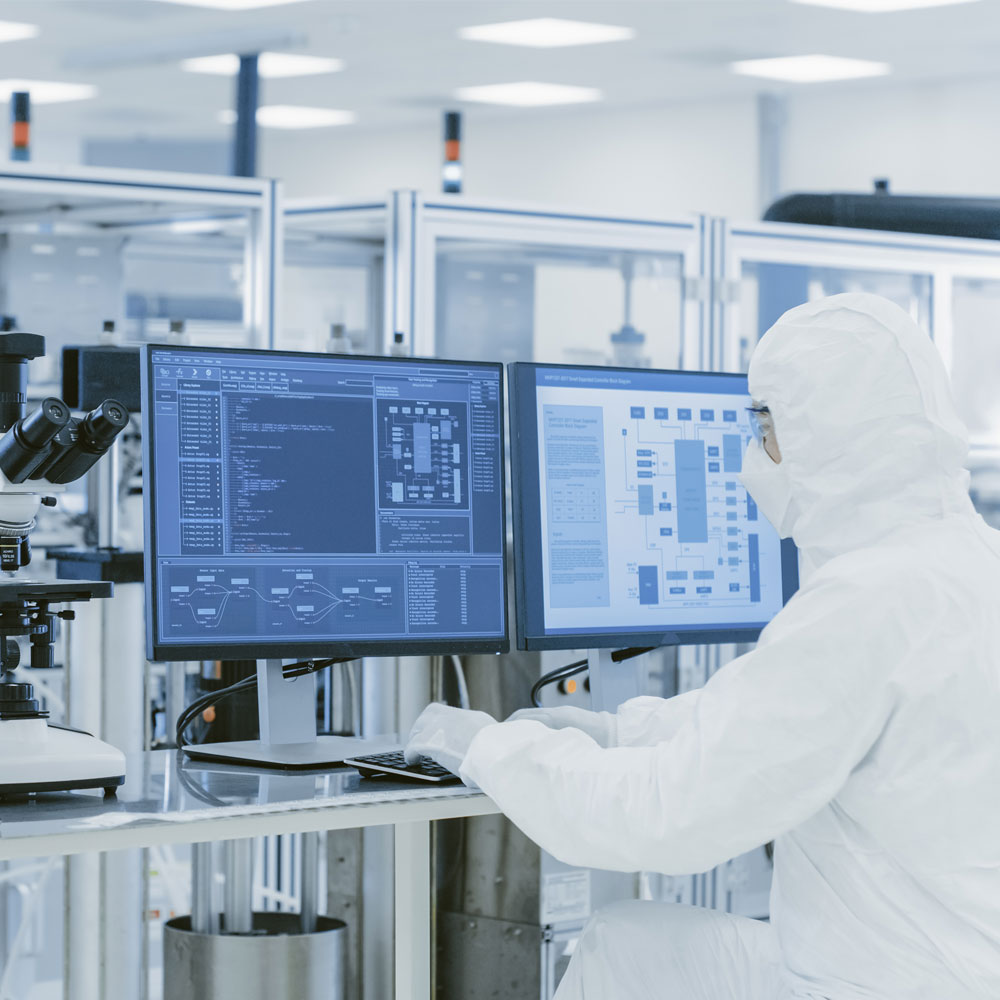 Scientist in protective suit working on computer with laboratory equipment in high-tech environment.