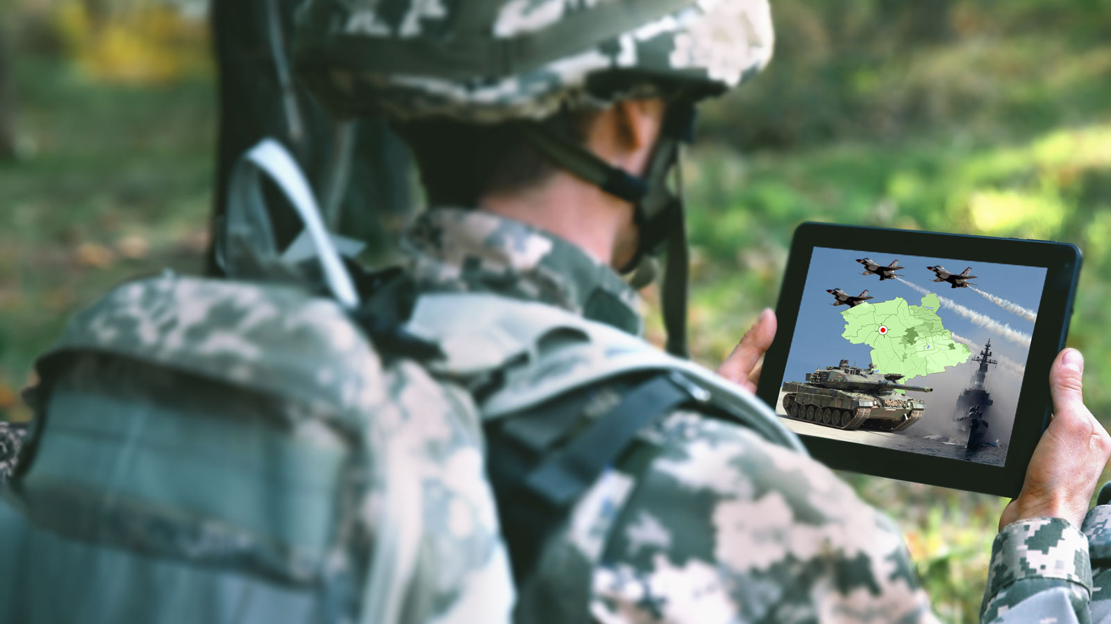 Soldier in camouflage uniform looking at a tablet showing military jets, tank, warship, and a map.